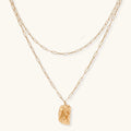 Layered gold paperclip chain necklace with organic sculptural pendant in warm lighting on cream background