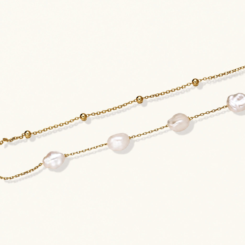 Double-strand gold bracelet with irregular baroque pearls and smooth freshwater pearls on cream background.