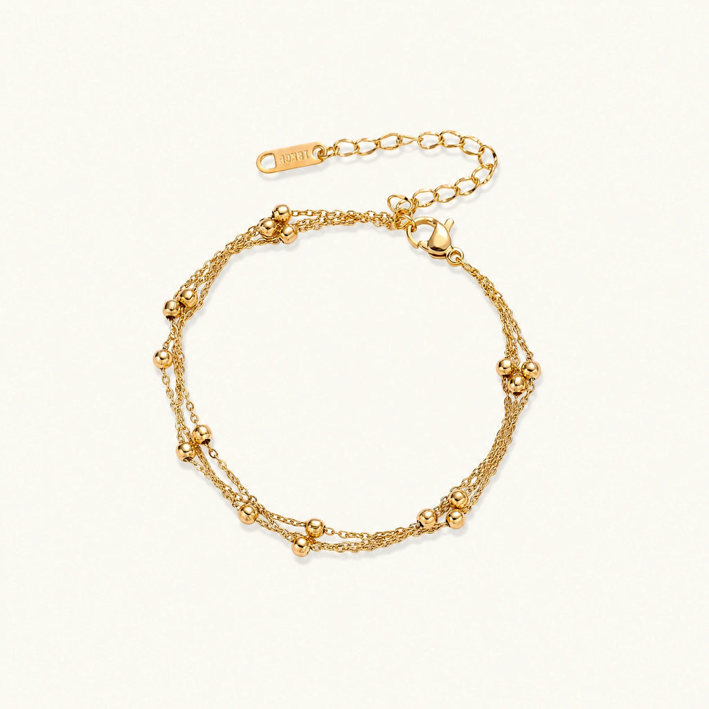 Three-strand gold-plated bracelet with clustered ball beads and adjustable clasp on cream background